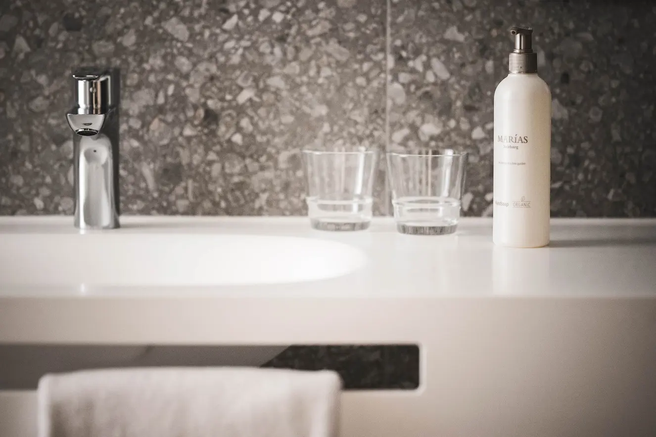 Modernes Badezimmerwaschbecken mit zwei klaren Gläsern, einem Seifenspender und einem Handtuch auf einer weißen Arbeitsplatte.